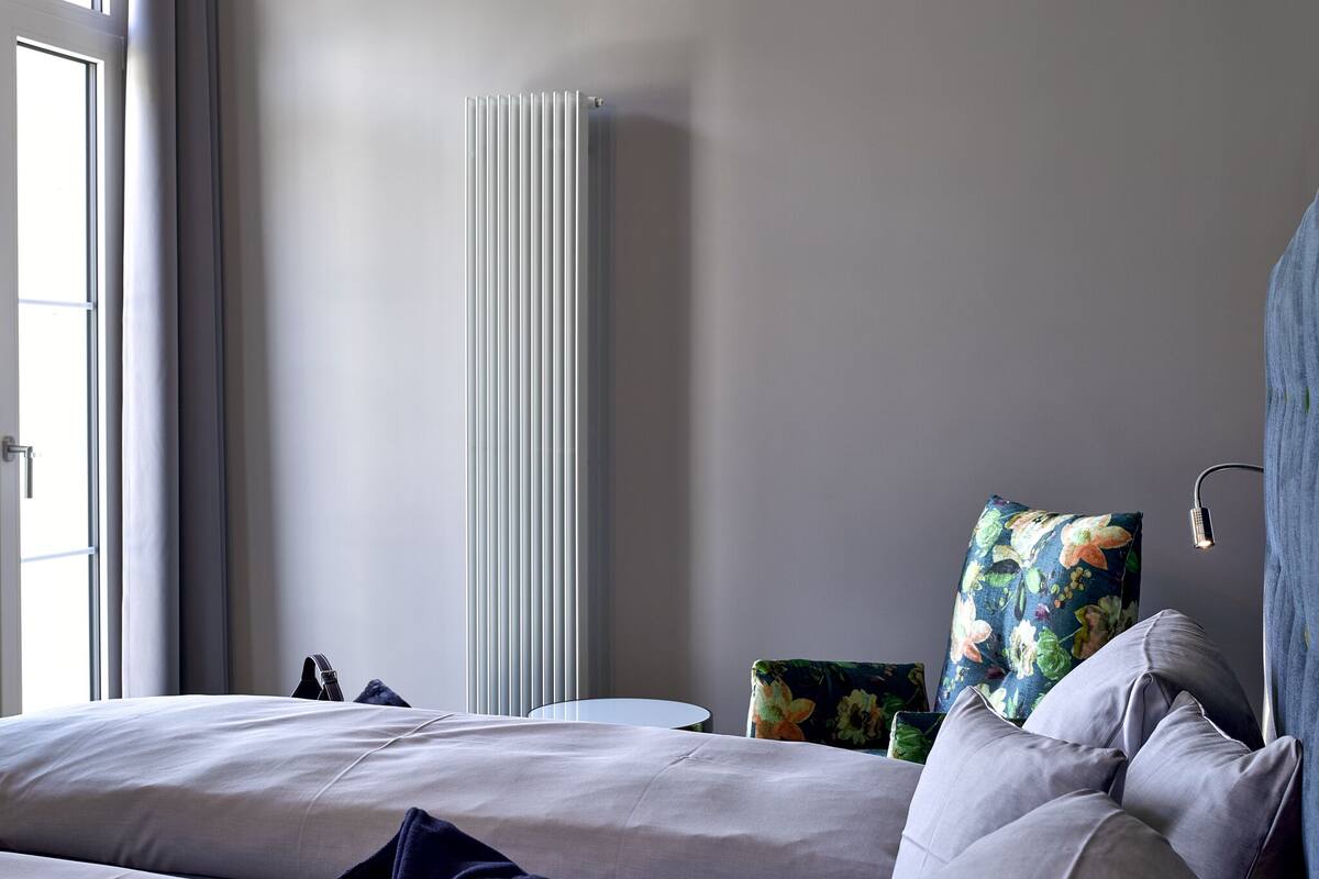 Una habitación de hotel moderna con una cama, un radiador, una mesita y una ventana.