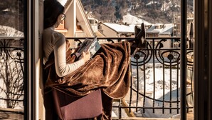 Una persona leyendo un libro en un balcón con vista a la montaña.