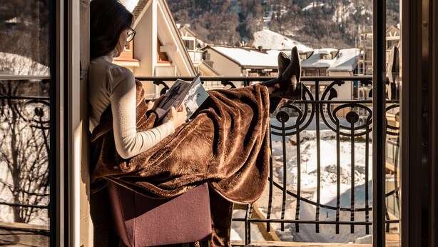 A person reading a book on a balcony with a mountain view. - Bellevue-Terminus - Urban Lifestyle Hotel (Engelberg)