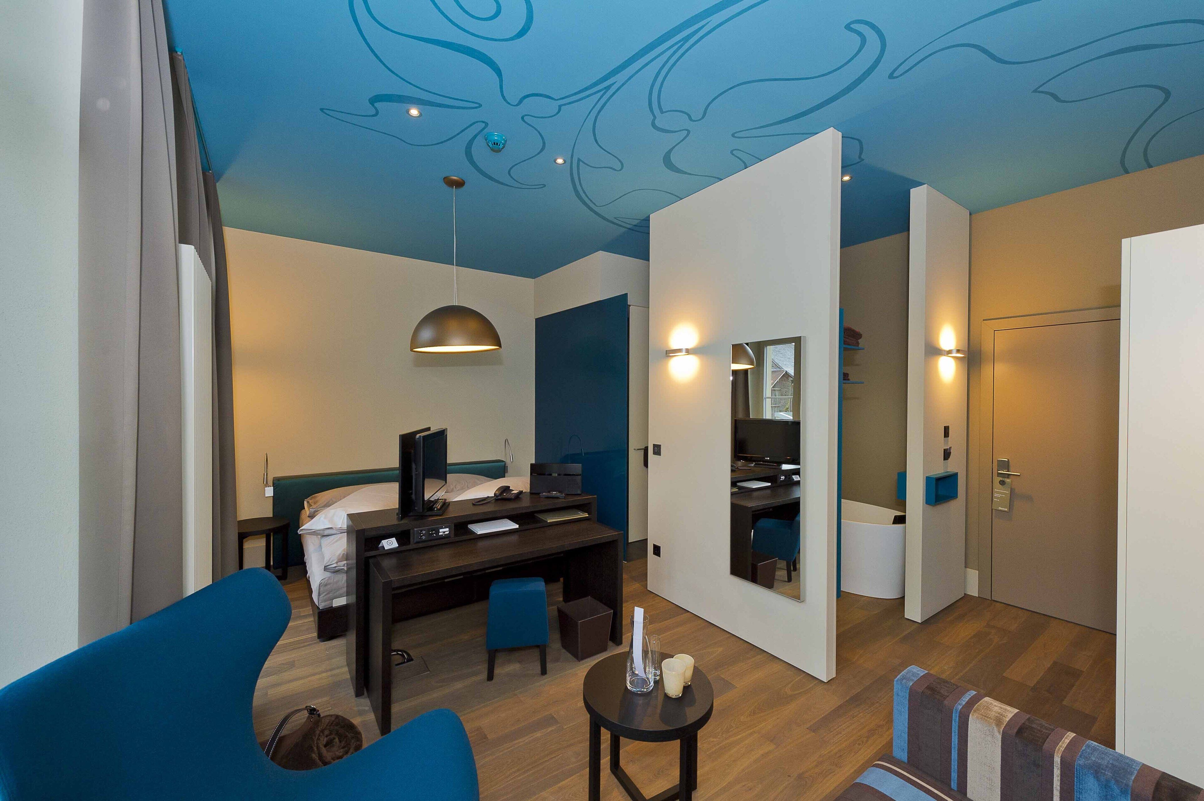 A modern hotel room with a bed, desk, and seating area.