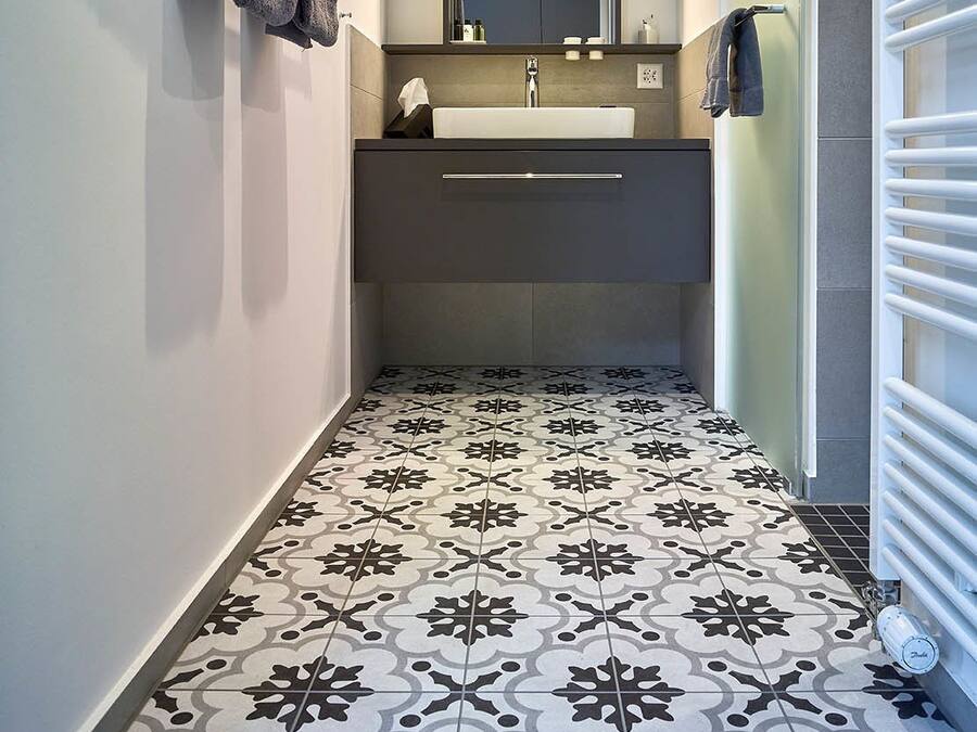 Moderni kylpyhuone, jossa on kuviollinen lattia, peilillä varustettu pesuallas ja pyyhkeet seinällä.