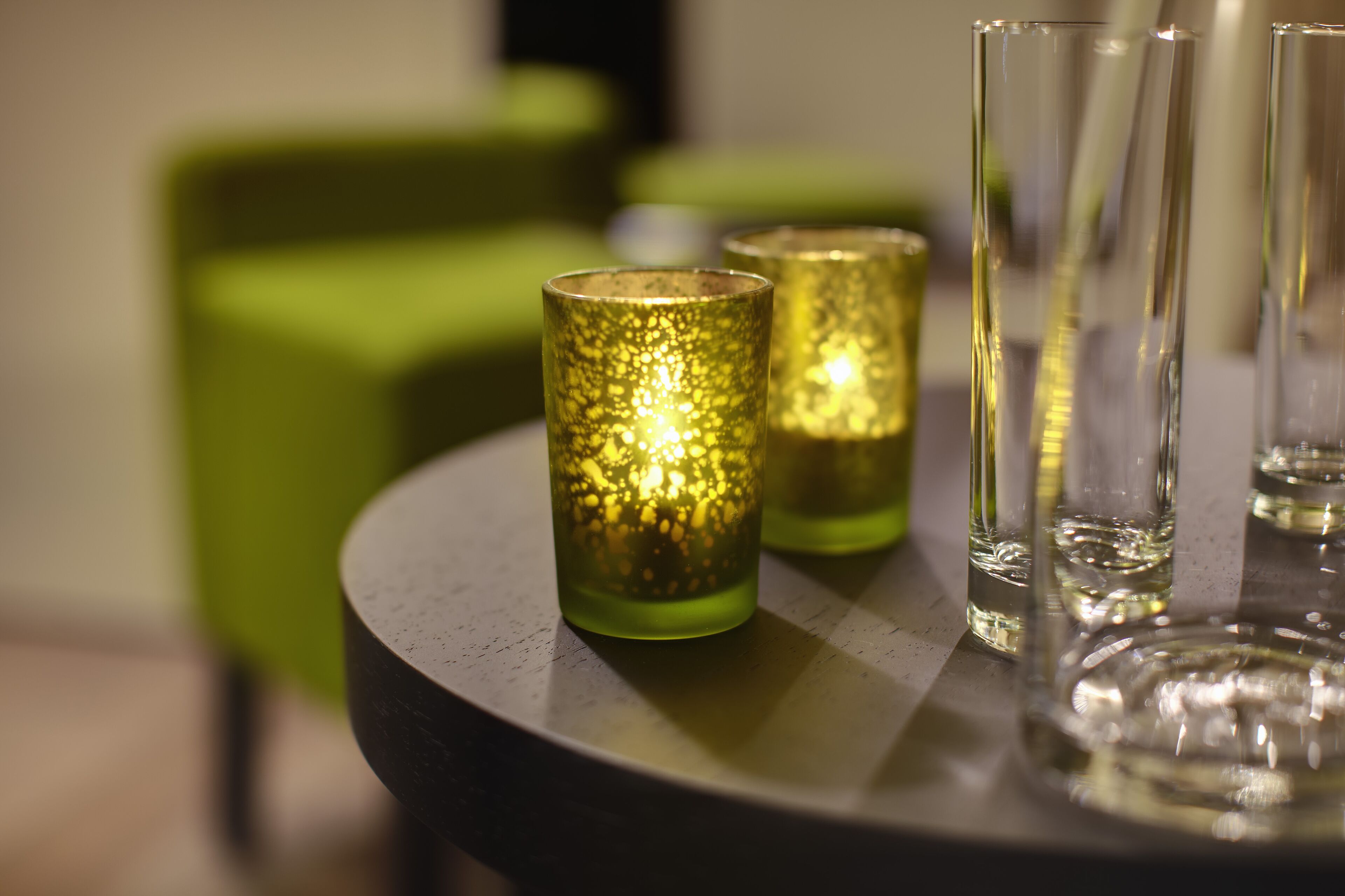 A table with three glass candle holders and a few empty glasses.