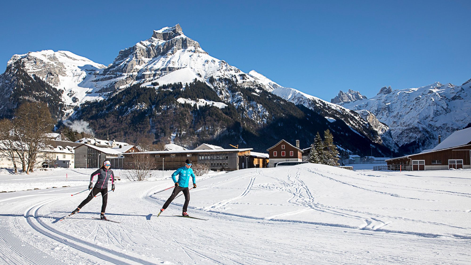 A ski resort with snow-covered slopes, wooden buildings, and a mountain backdrop.