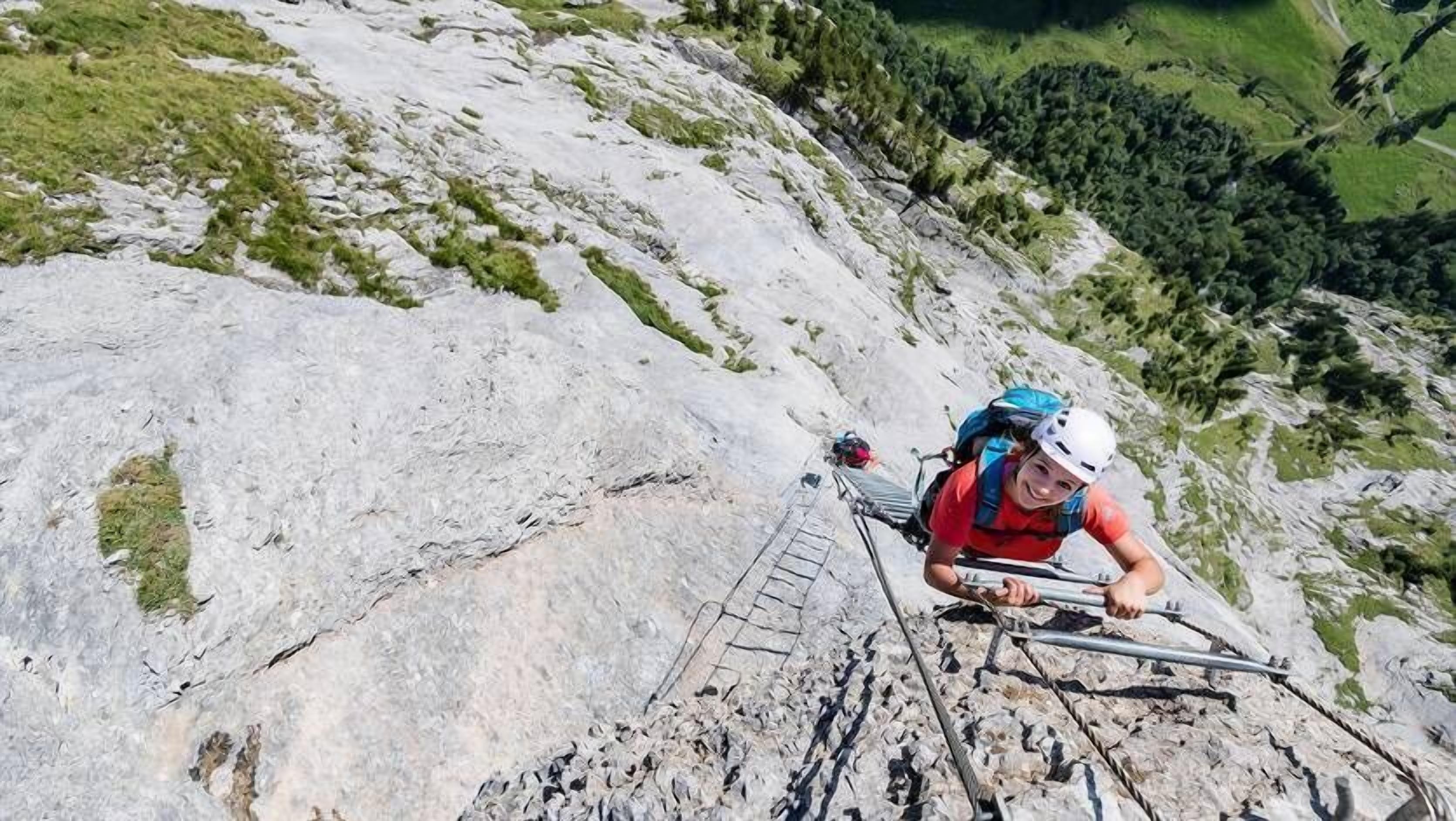 A person climbing a rocky mountain path with a metal ladder.