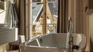 A modern bathroom with a freestanding bathtub, a mirror, and a view of a mountain landscape through a glass door. - Bellevue-Terminus - Urban Lifestyle Hotel (Engelberg)