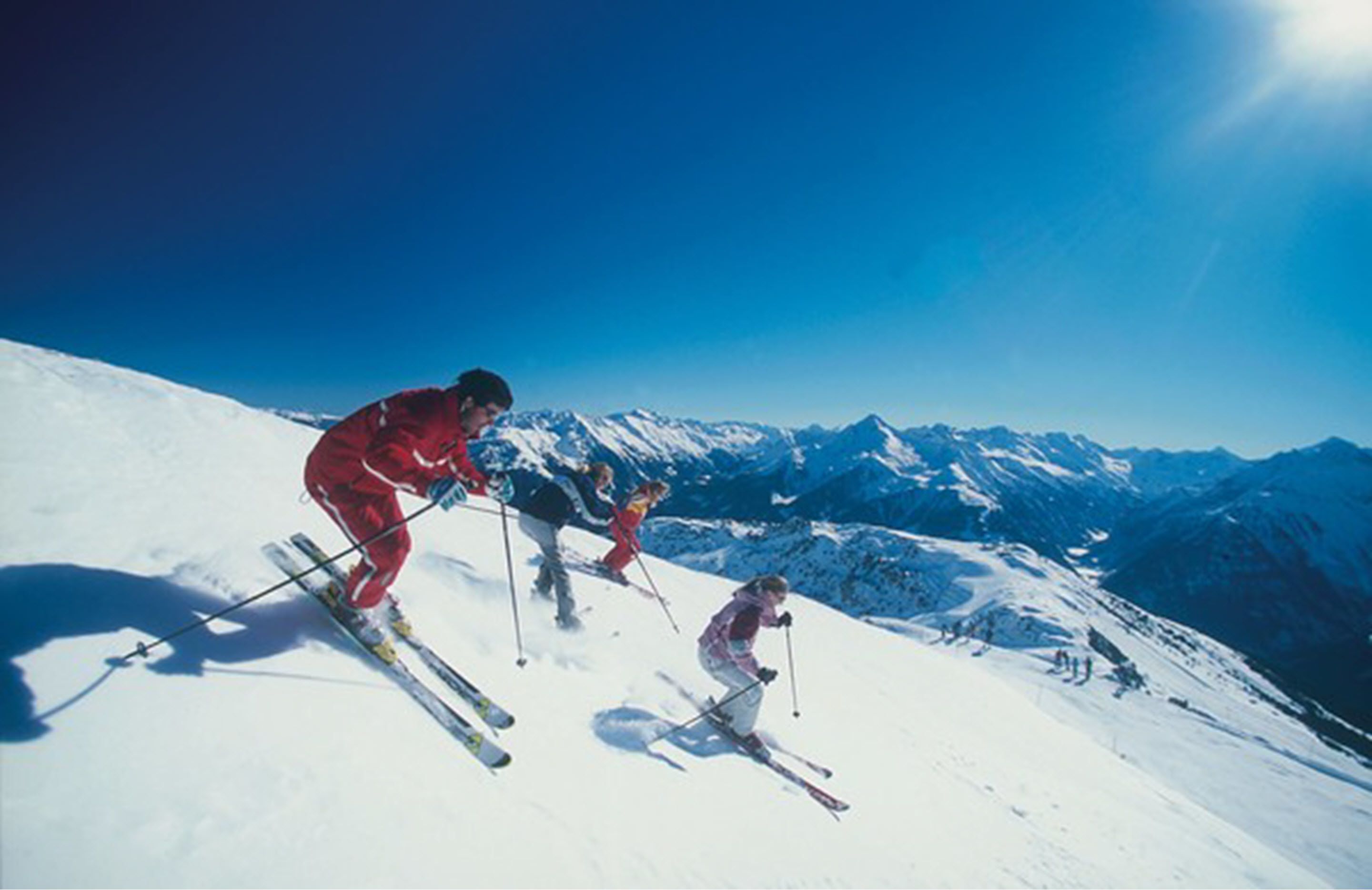 Skiers on a snowy mountain slope with a clear blue sky.