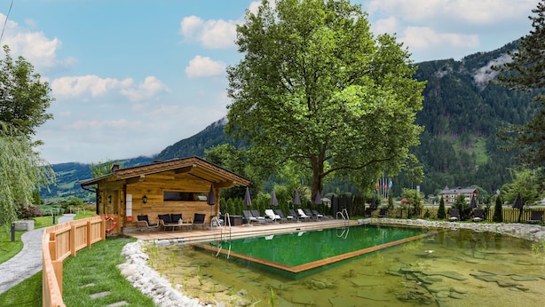 Une cabane en bois avec une piscine, entourée d’une clôture en bois, d’arbres et, au loin, de montagnes.