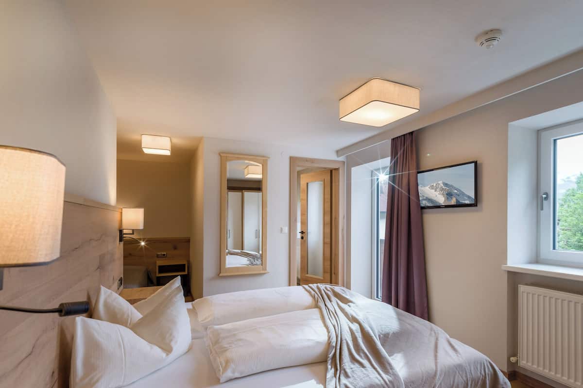 Una habitación de hotel con cama, lámparas de noche, un espejo, una ventana con cortinas y un radiador.