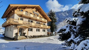 Un chalet en bois à plusieurs étages, doté de balcons, qui se dresse sur fond de montagnes enneigées.