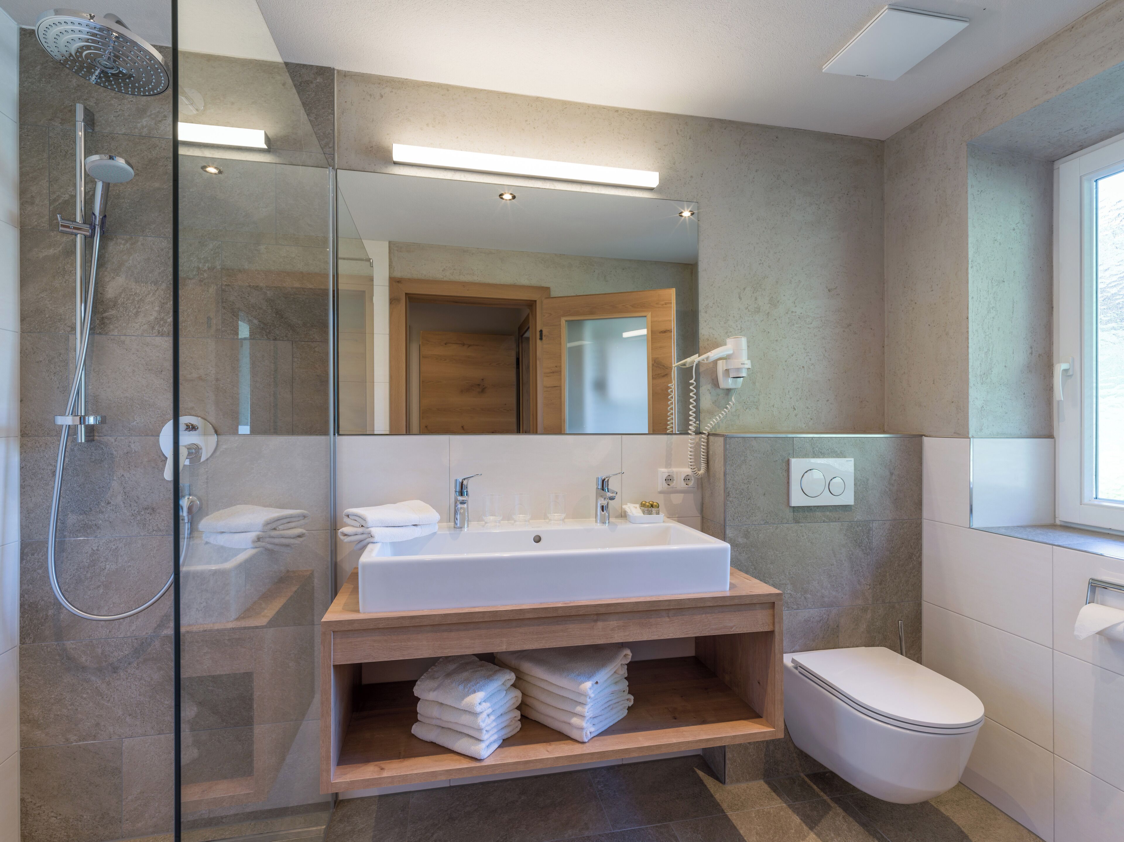 A modern bathroom with a glass-enclosed shower, a white sink, and a toilet.