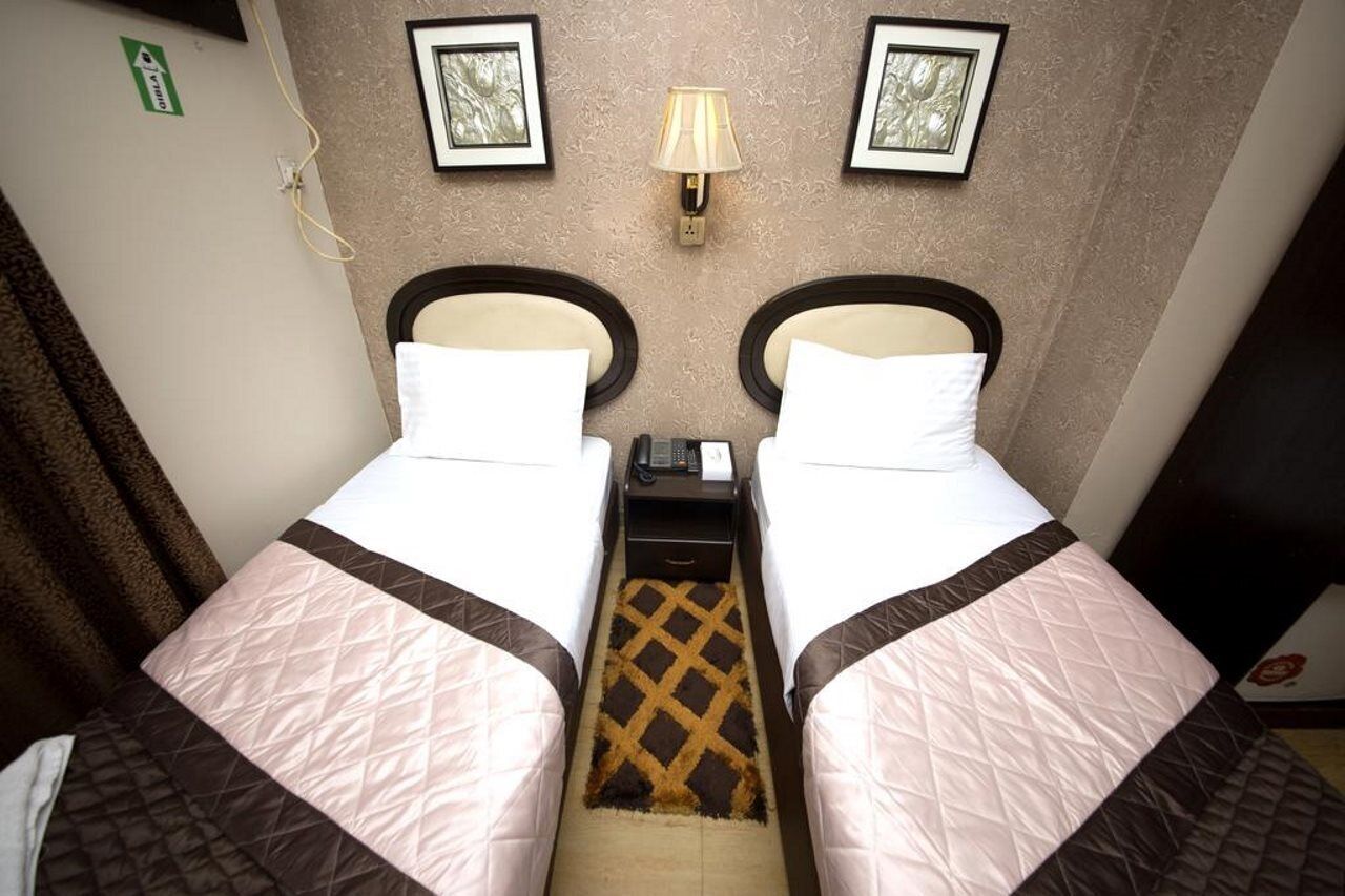 A twin room with two beds, a nightstand, a lamp, and framed pictures on the wall.