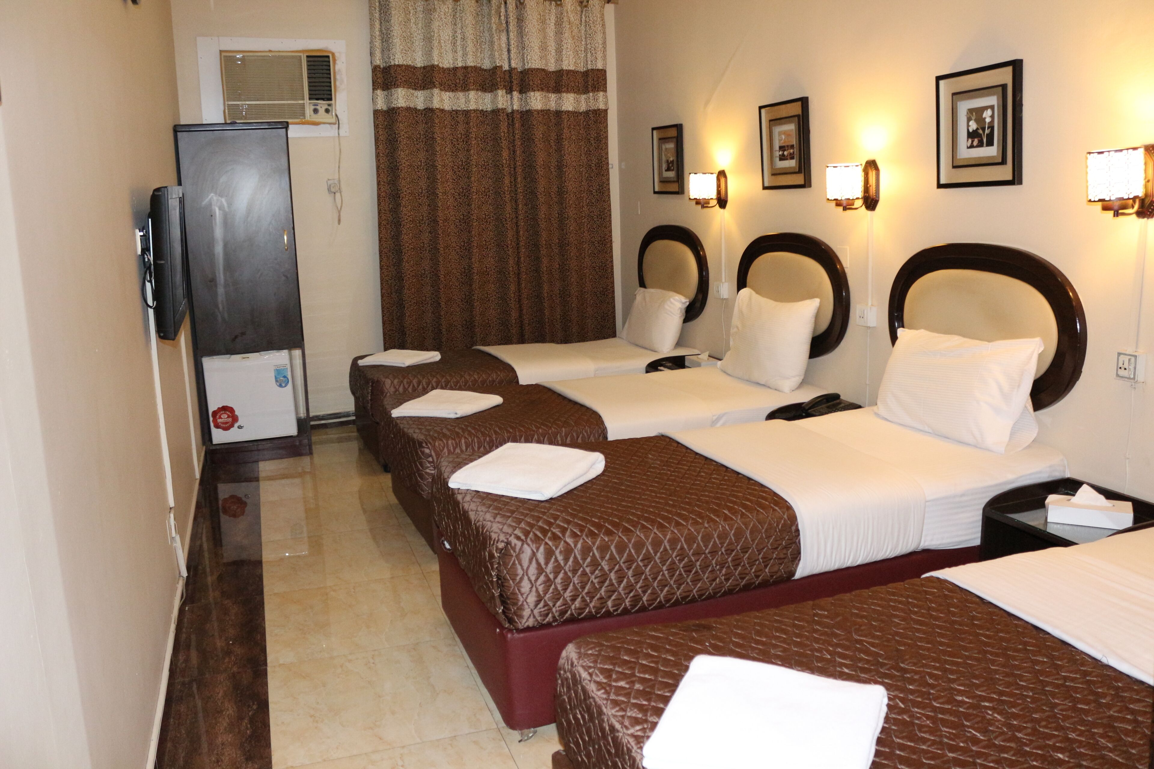 A hotel room with three beds, a television, and wall-mounted lighting.