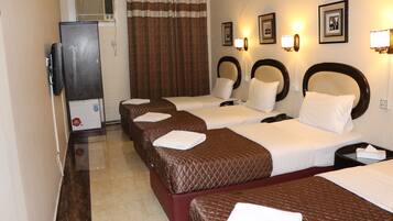 A hotel room with three beds, a television, and wall-mounted lighting.