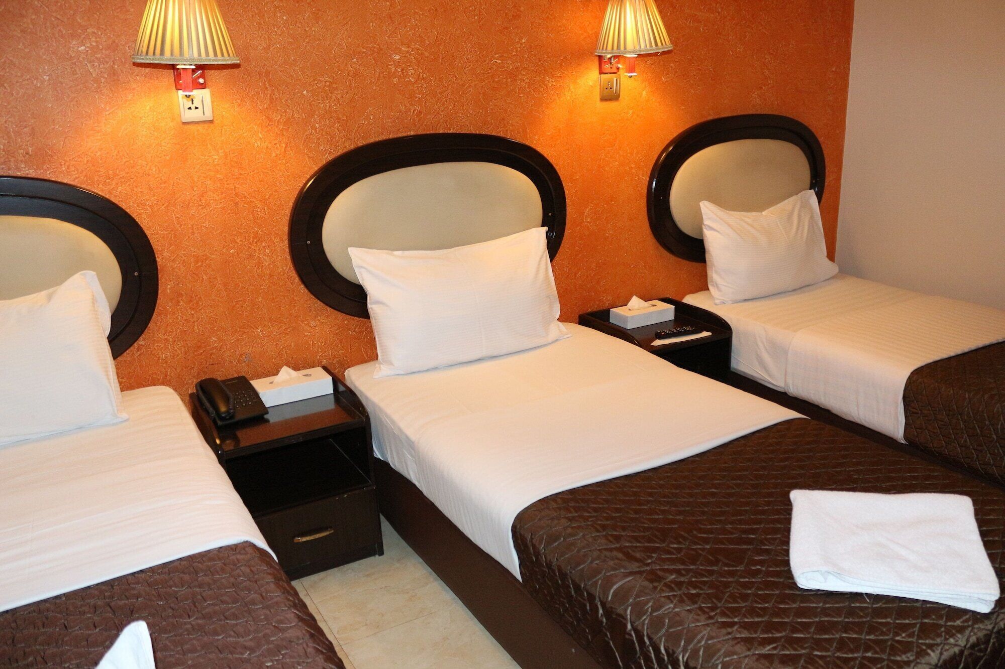 Ein Hotelzimmer mit drei Betten, jeweils mit Kopfteil, Nachttisch und Lampe.