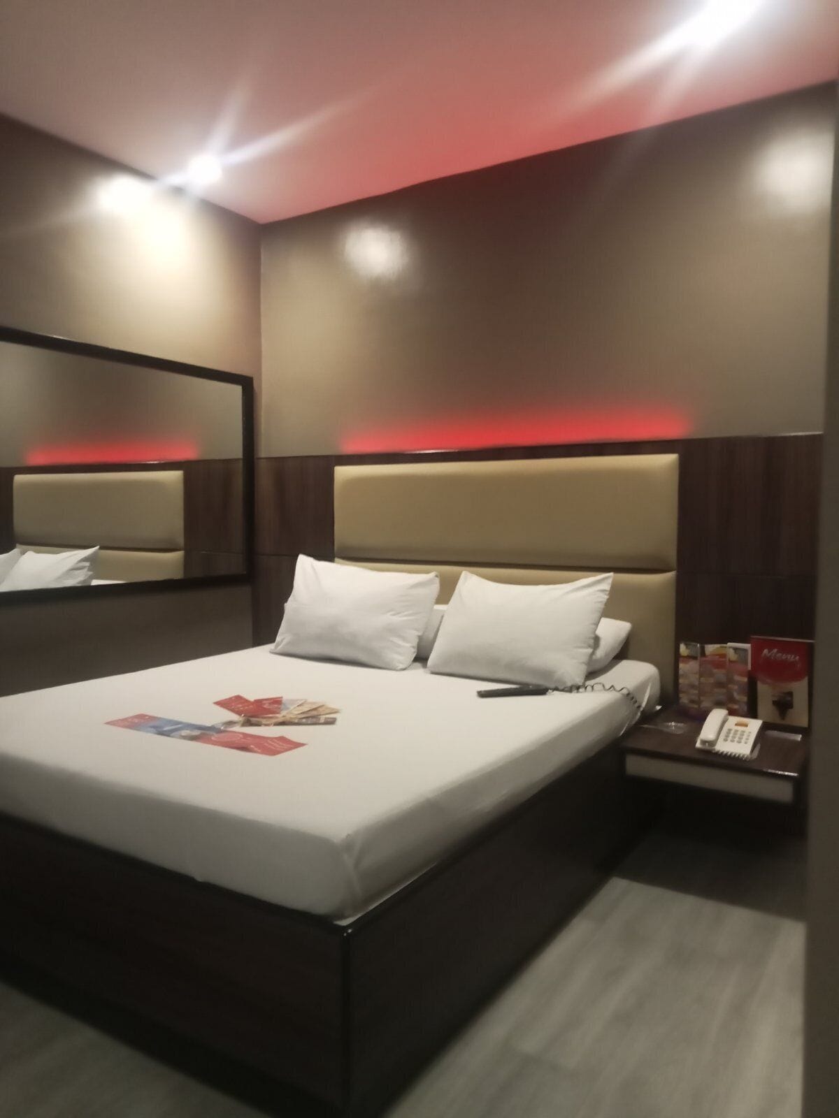 A hotel room with a large bed, a bedside table with a phone and a menu, and a mirror on the wall.