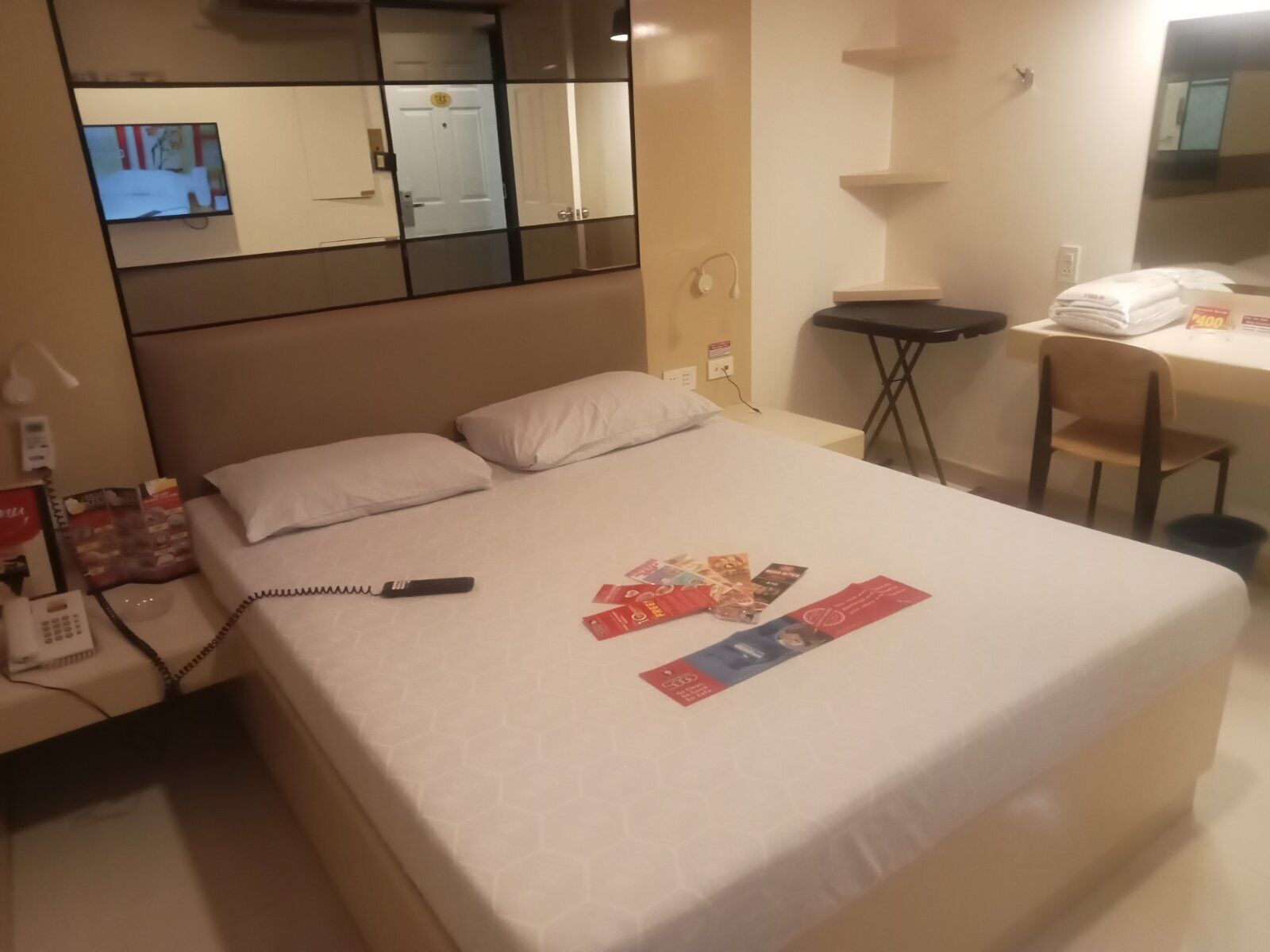A hotel room with a bed, a desk, a chair, a telephone, and a TV.