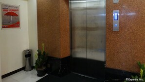An elevator with a marble wall, a trash bin, and a potted plant.