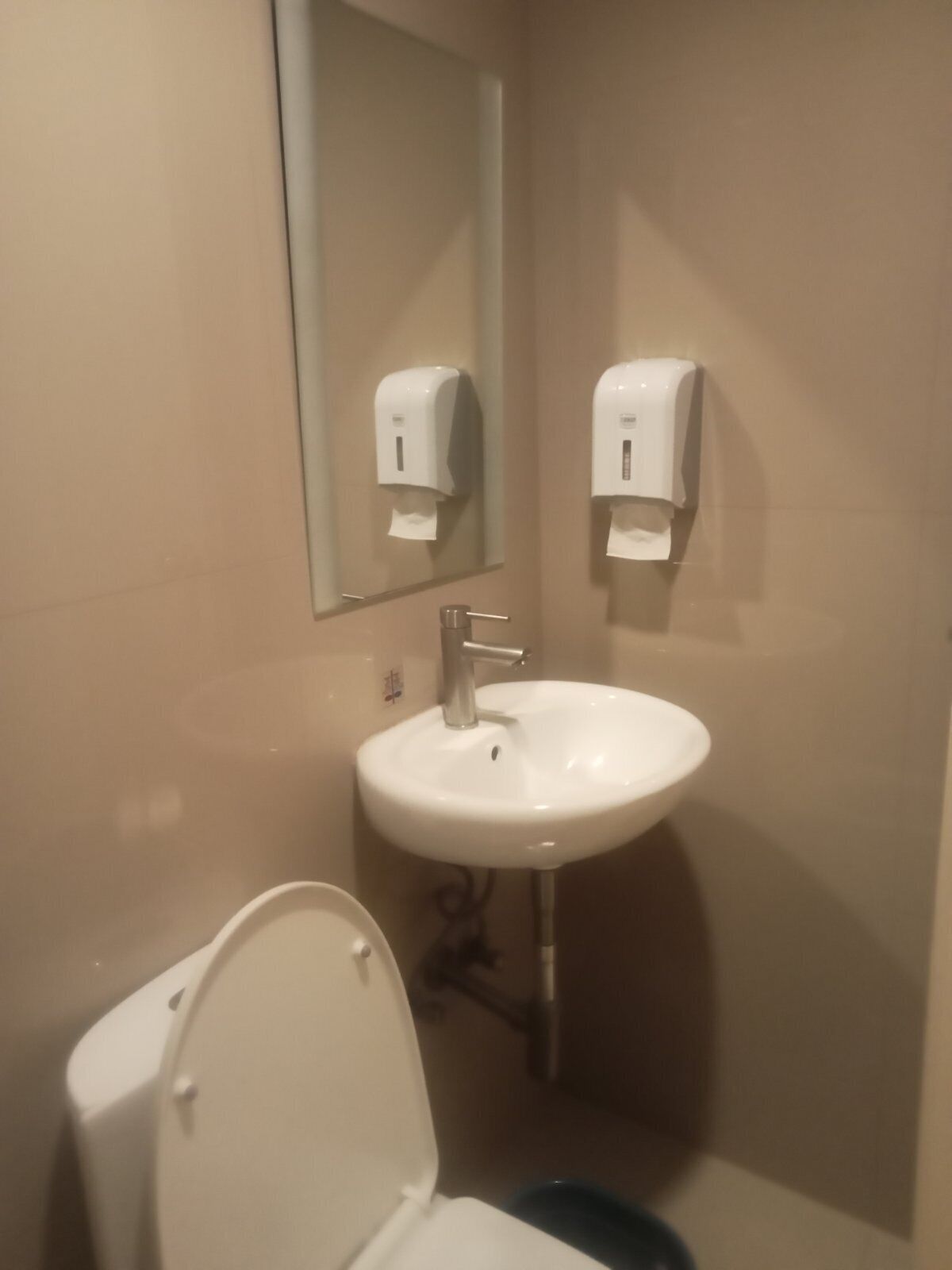 A bathroom with a white sink, a mirror, and two paper towel dispensers.