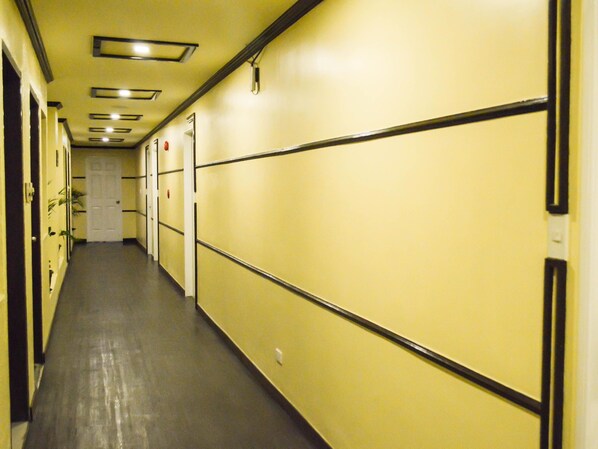 Un long couloir étroit aux murs jaunes et aux moulures noires, qui mène à une porte au fond.