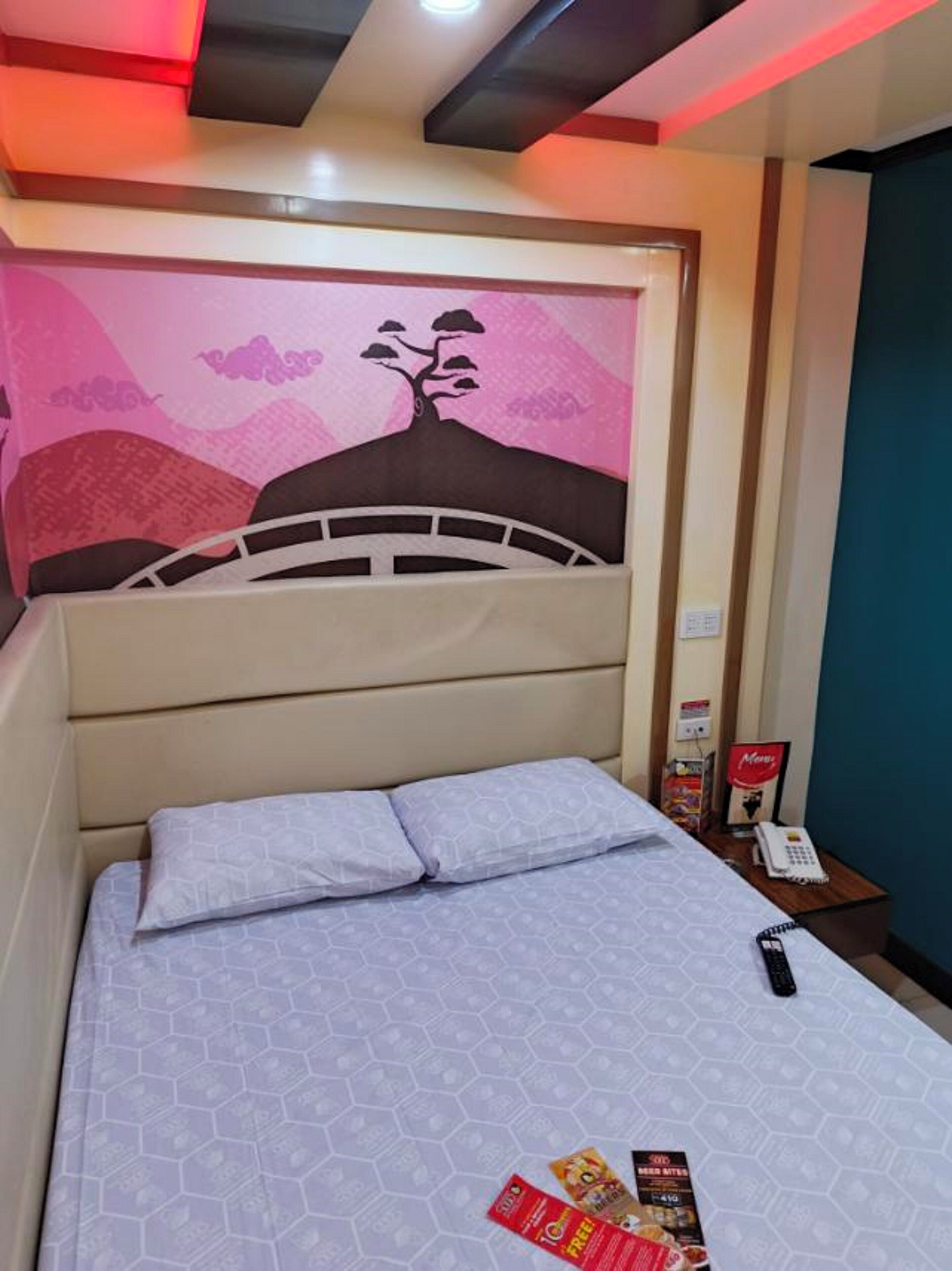 A neatly made bed with a patterned bedspread, a headboard with a decorative wall art, and a bedside table with a phone and some items.