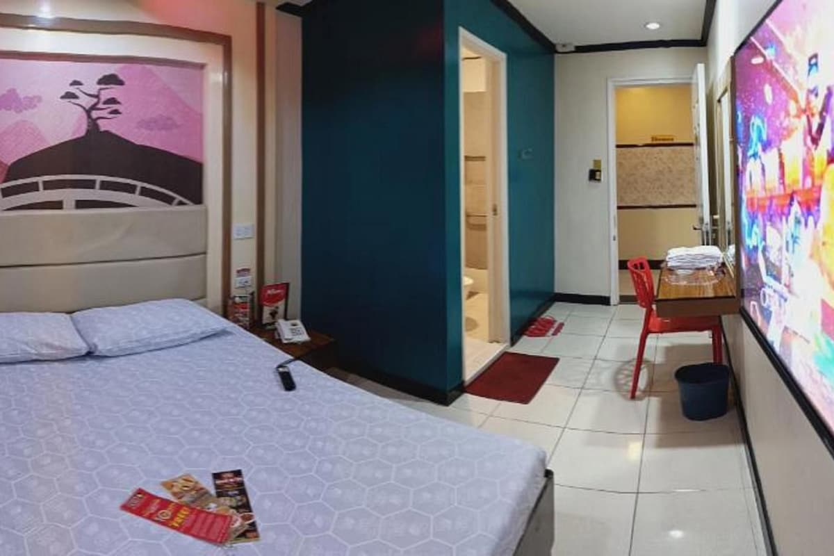 A hotel room with a bed, a wall with a mural, a desk with a chair, and a bathroom visible through an open door.