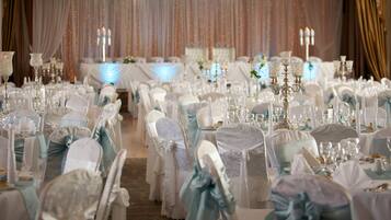 A banquet hall with rows of tables set for a formal event, each with white tablecloths and chairs adorned with light blue sashes.