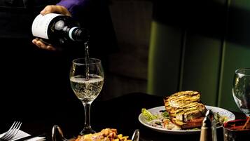 A person pouring wine into a glass on a table with plates of food and a salt shaker.