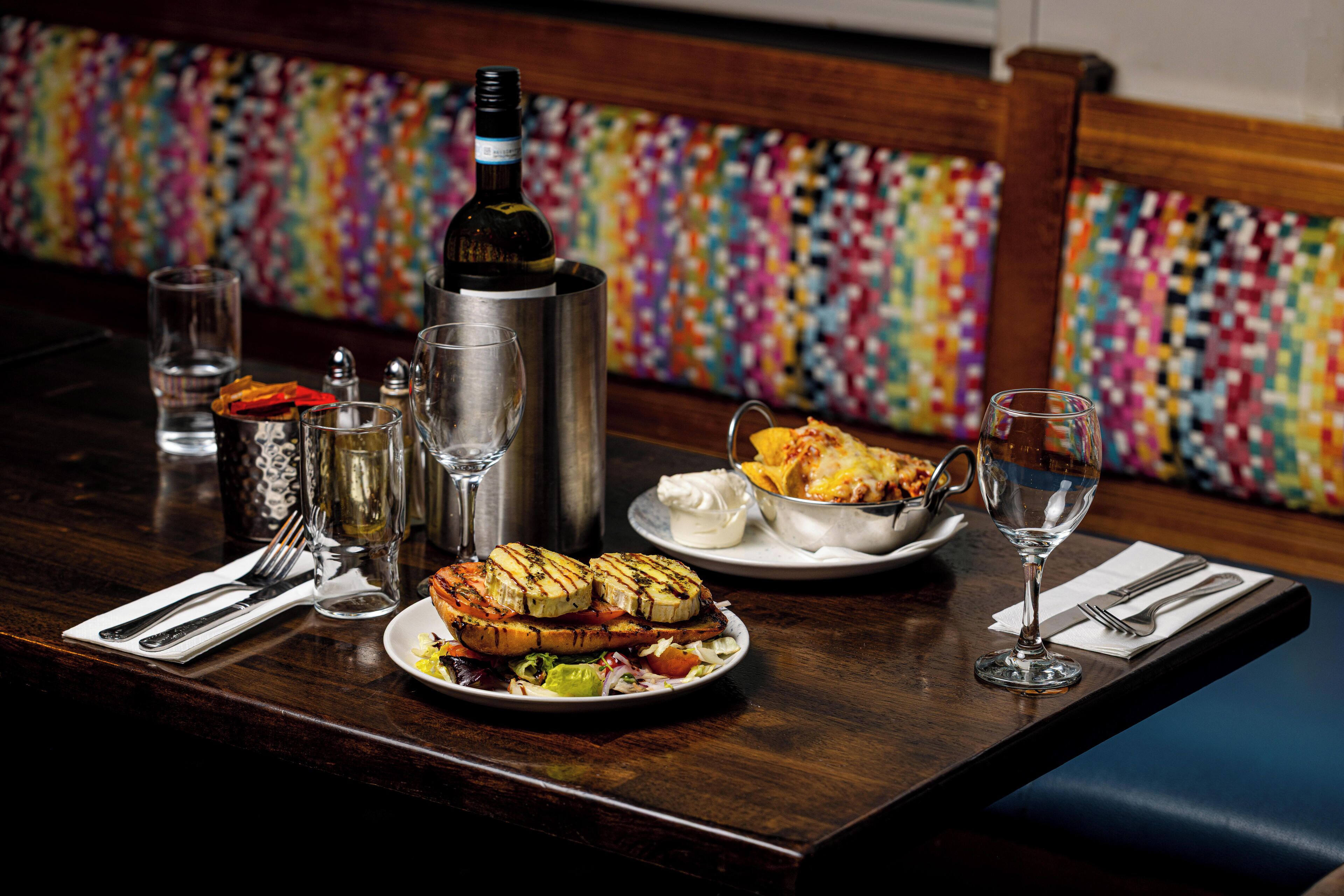 A dining table with a bottle of wine, a thermos, and plates of food.
