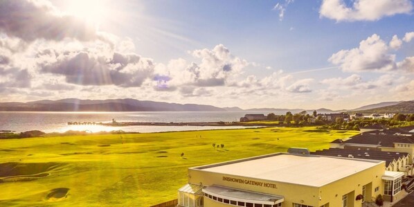 The Inishowen Gateway Hotel met uitzicht op een golfbaan en een waterlichaam op de achtergrond.