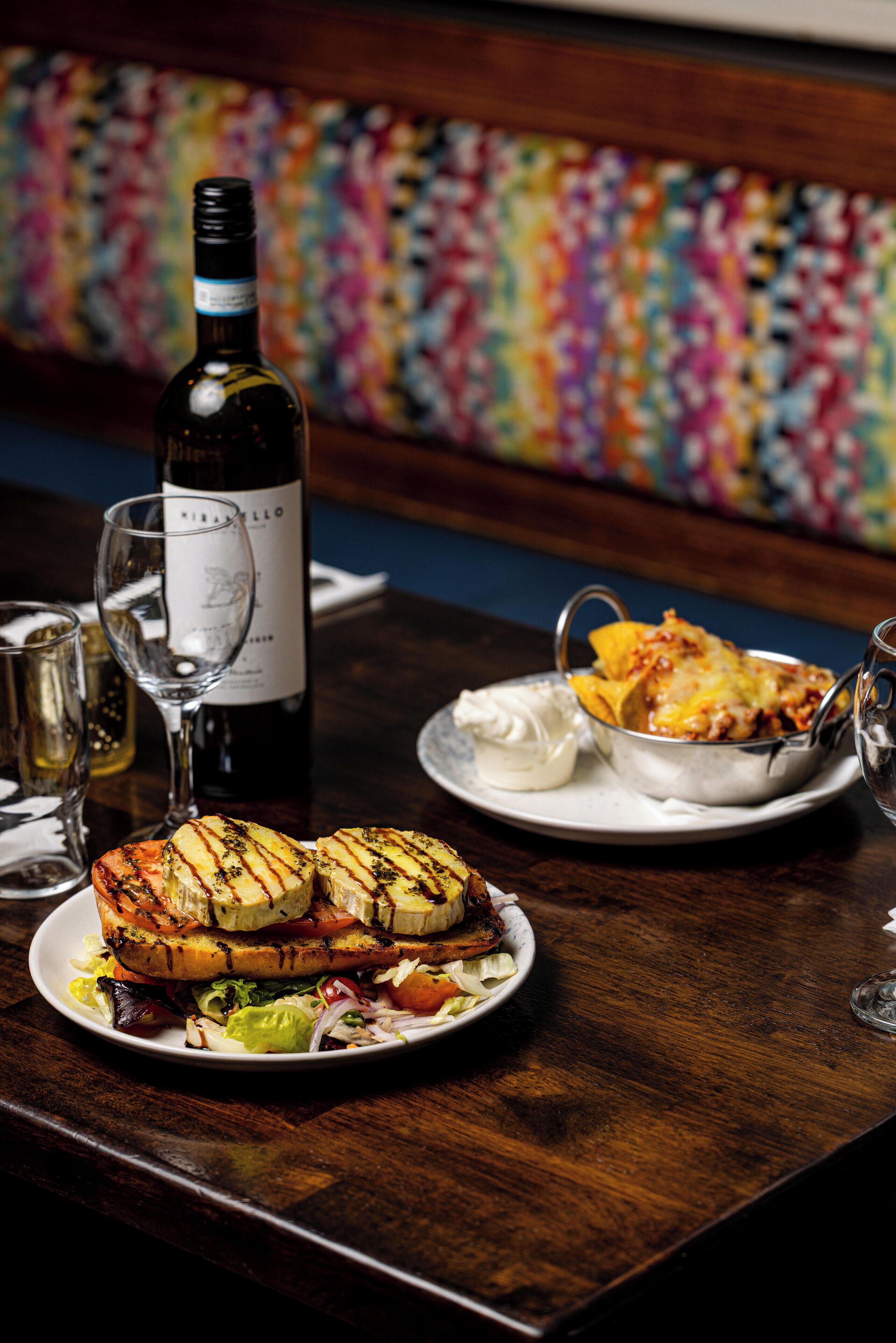 A dining table with a bottle of wine, a glass, and a plate of food.