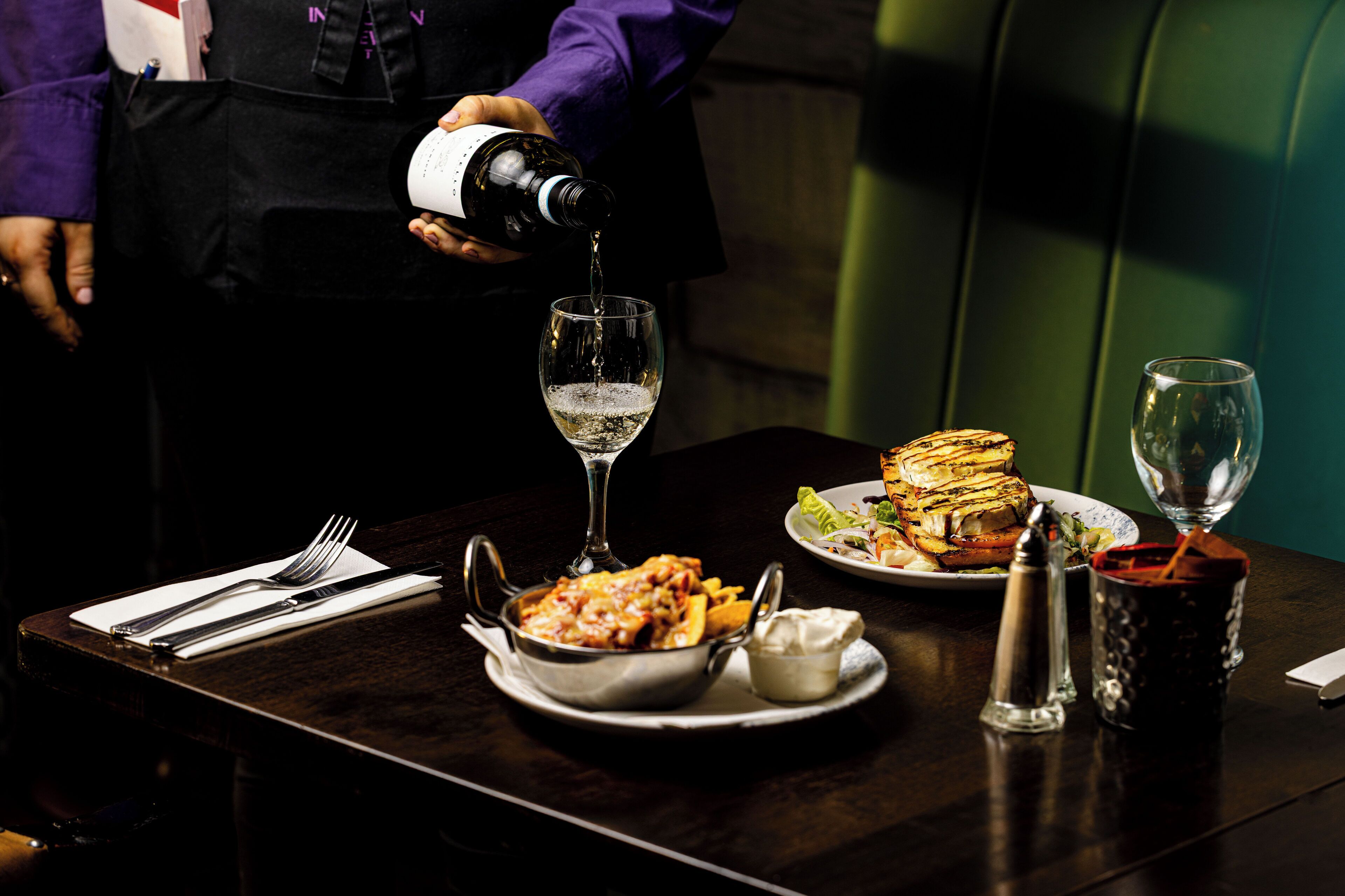 A table set with a meal, a wine glass, and a bottle being poured into another glass.