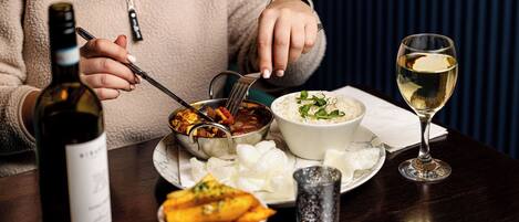 A person dining at a table with a bottle of wine, a bowl of rice, a glass of white wine, and a bowl of fried food.