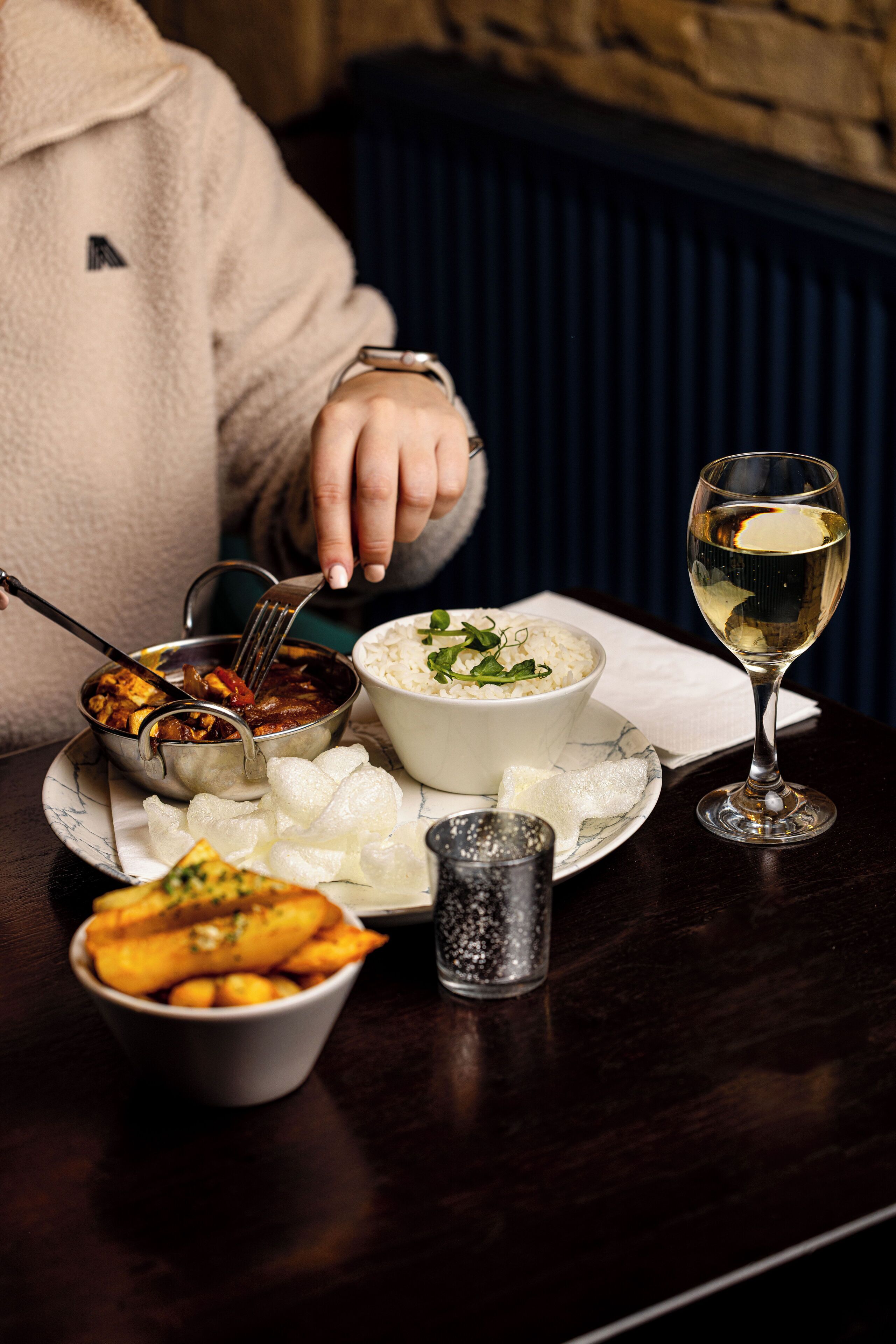 A dining table with a bowl of rice, a glass of white wine, and a bowl of soup.