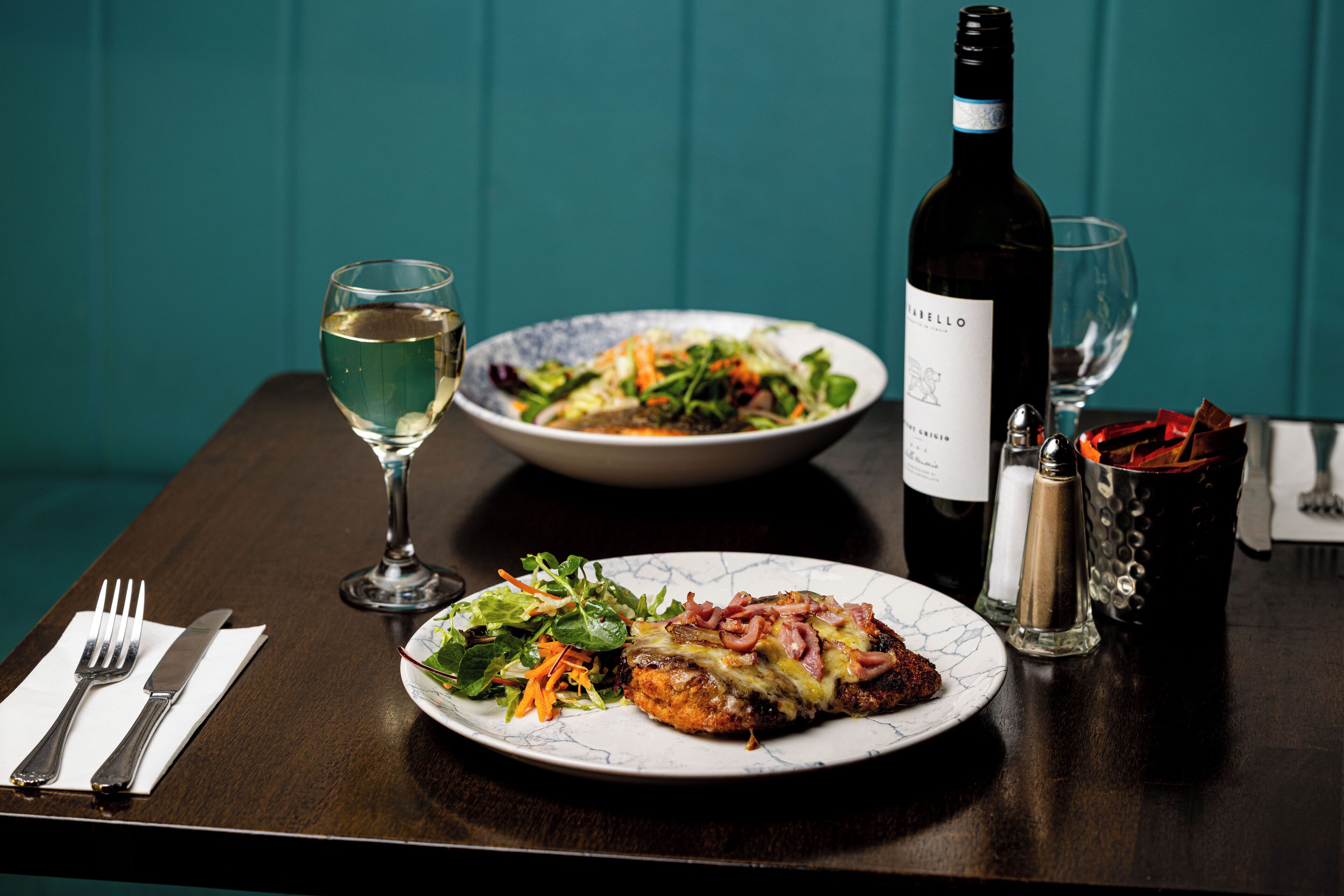 A dining table with a plate of food, a bottle of wine, and a glass of wine.