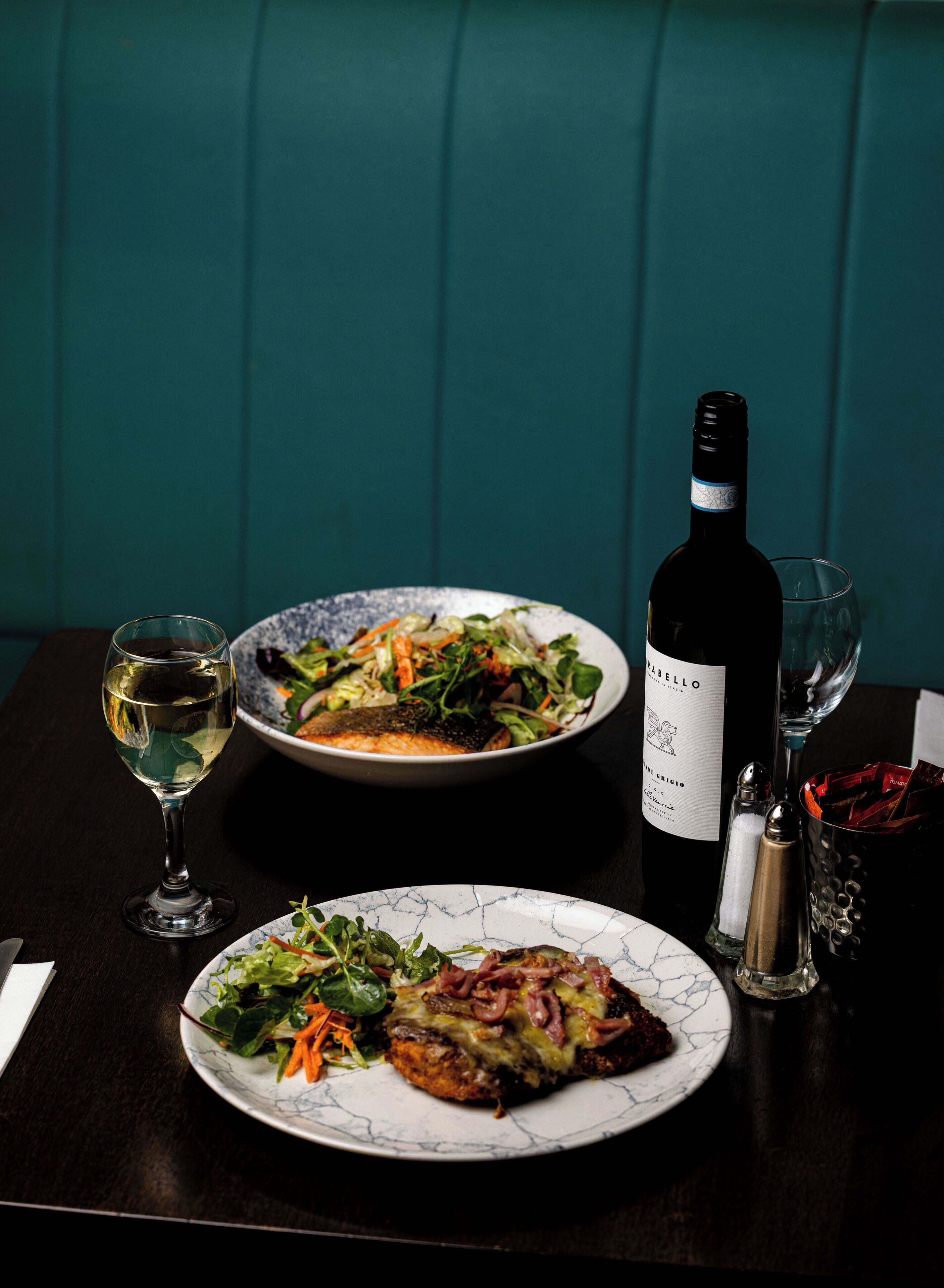 A table with two plates of food, a bottle of wine, and two glasses.