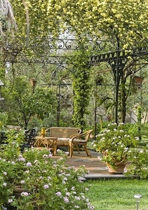 A garden with a wrought iron archway, a wooden bench, and potted plants. - Chalet Lidia (Sorrento)