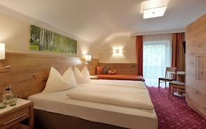 A hotel room with a large bed, a desk with a chair, a wooden wardrobe, and a painting on the wall.