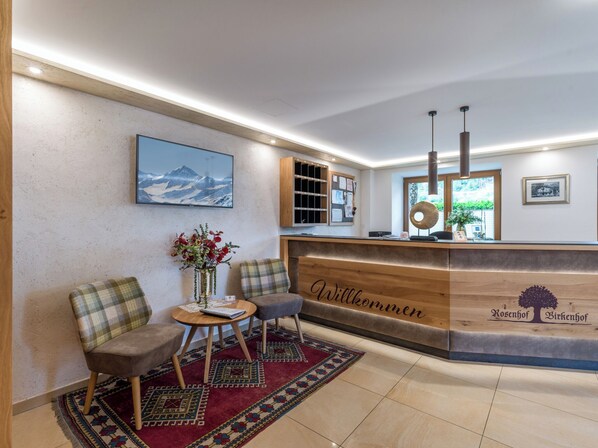 A reception area with a wooden reception desk, a mounted television, a bulletin board, and a seating area with a rug. - Gästehaus Birkenhof (Mayrhofen)