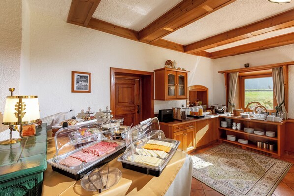 A buffet setup with various food items, wooden cabinets, and a view of the outdoors. - Gästehaus Birkenhof (Mayrhofen)
