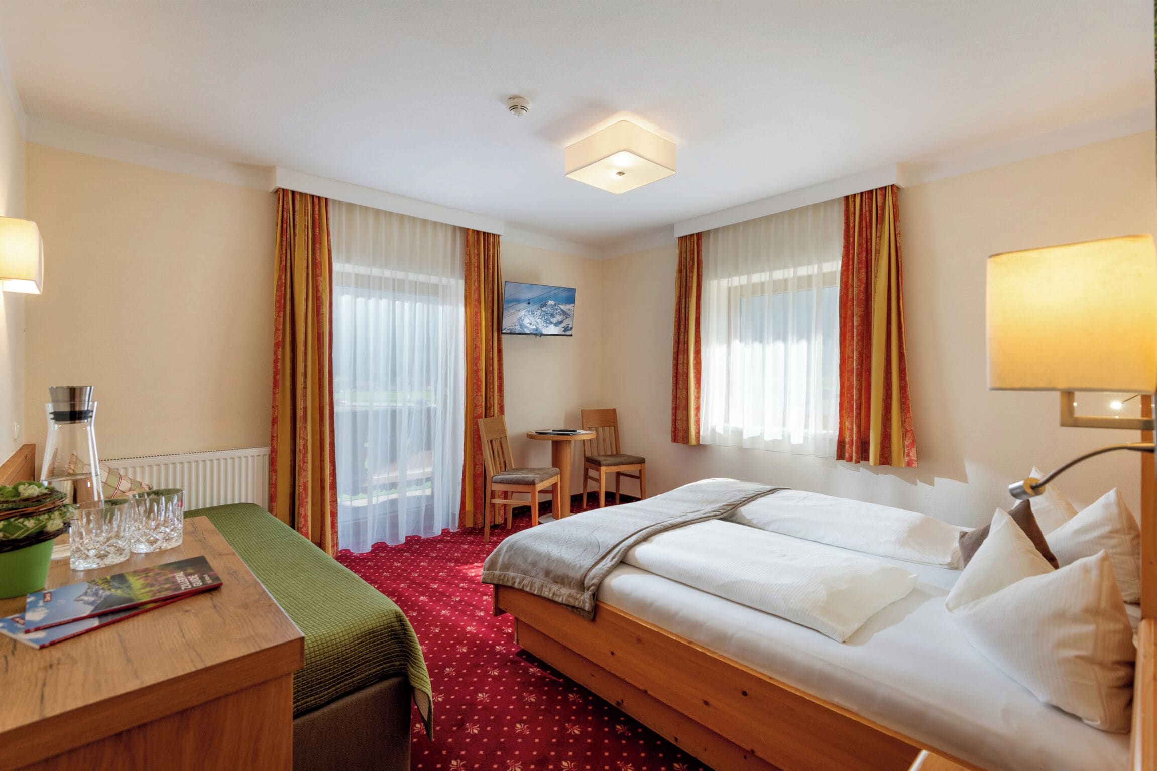 Camera d'albergo con un letto, una scrivania con lampada, una sedia, un tavolino e vista all'esterno dalla finestra.