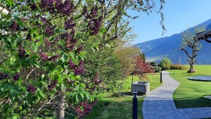 A wooden cabin with a stone foundation, a paved pathway, and a view of mountains in the background.