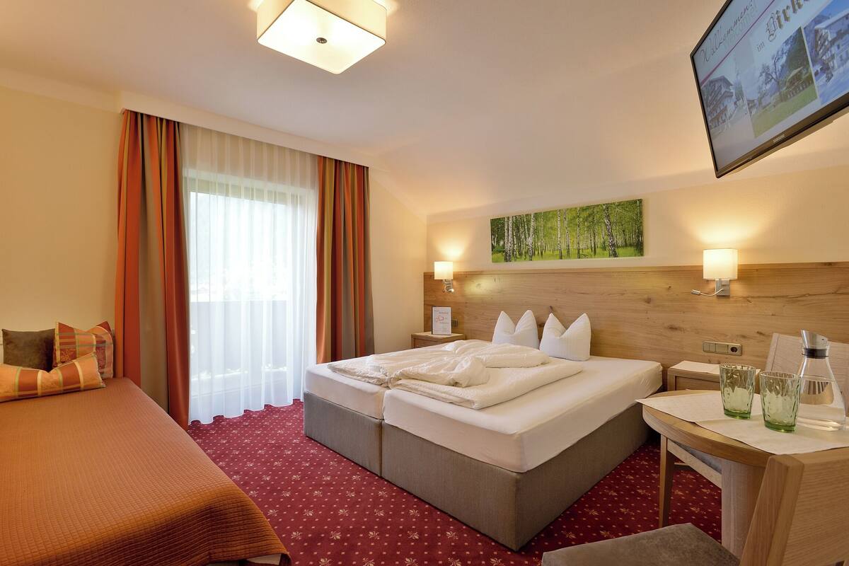 Een hotelkamer met een groot bed, een kleiner bed, een bureau met een lamp en een schilderij aan de muur.