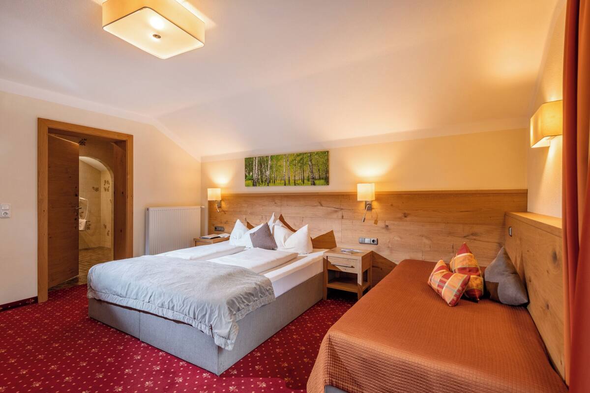 Een hotelkamer met een groot bed, een kleiner bed, een houten hoofdbord, een nachtkastje, een wandlamp en een schilderij boven het bed.