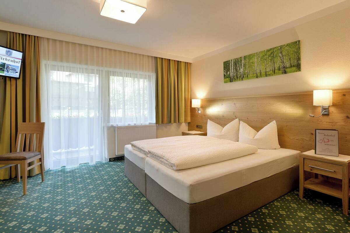 Hotelkamer met groot bed, twee nachtkastjes, een stoel, een televisie en een schilderij aan de muur.