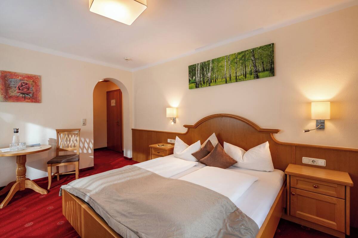 Een hotelkamer met een groot bed, twee nachtkastjes, een bureau met stoel en een schilderij aan de muur.