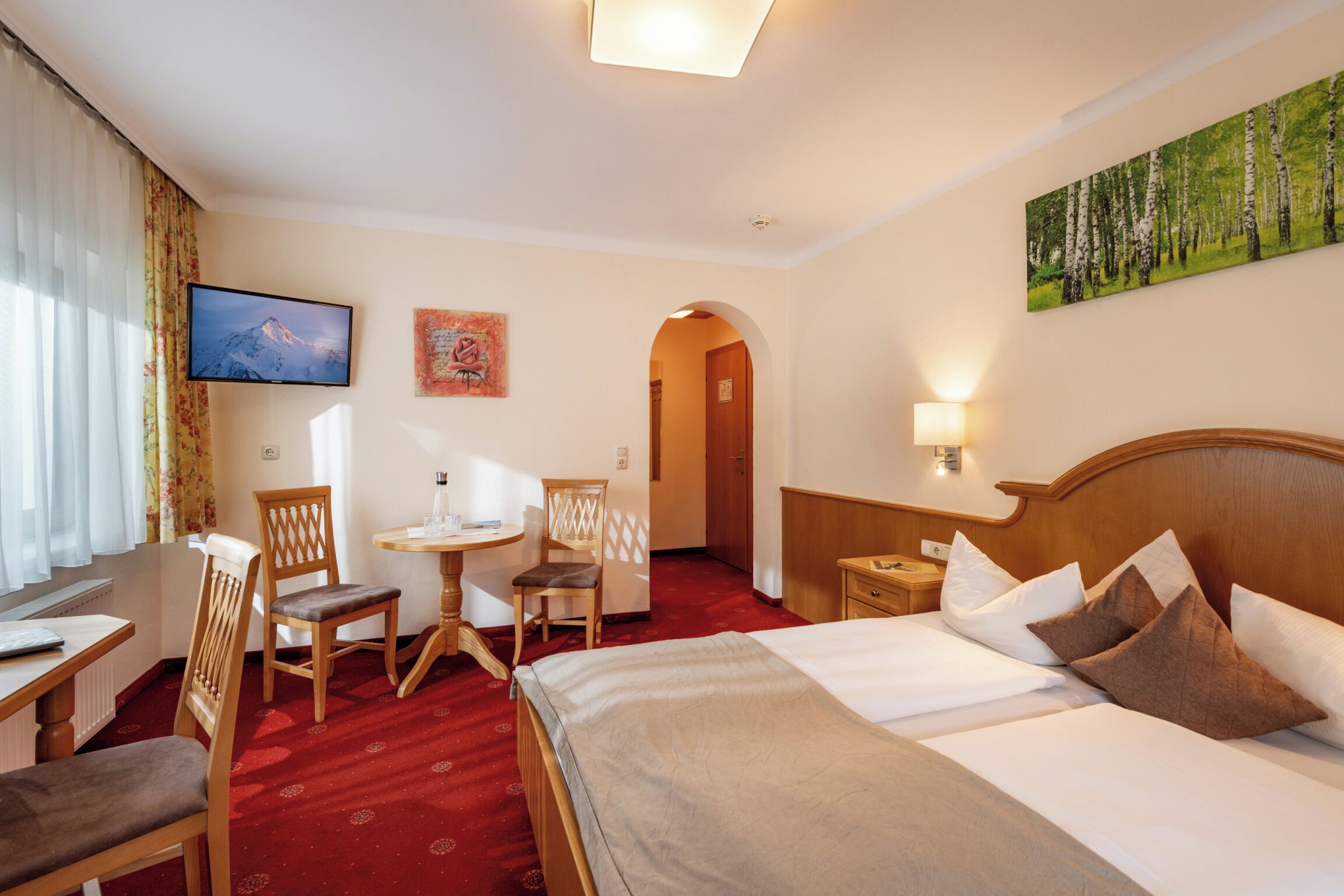 A hotel room with a large bed, a desk with a chair, a television, and a painting on the wall.