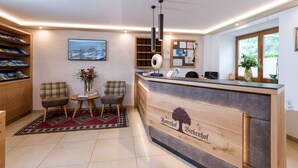 A reception area with a wooden desk, two chairs, a small table with a vase, and a bookshelf.