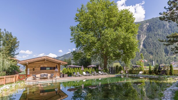 A wooden cabin with a pool, surrounded by trees and mountains.