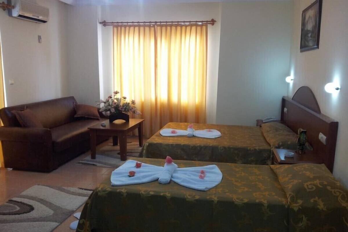 A hotel room with two beds, a sofa, a small table with a vase of flowers, and a window with curtains.