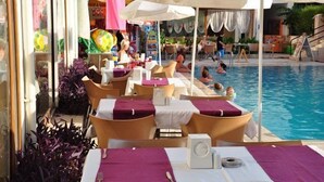 A poolside area with lounge chairs and tables, a pool, and a slide. - Inside Hotel (Manavgat)
